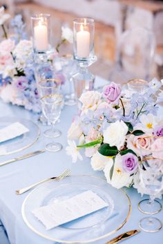 the table is set with white and purple flowers, silverware, and gold rimmed place settings