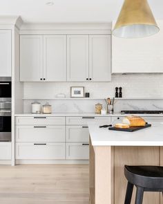 a kitchen with white cabinets and an island in the middle is lit by a pendant light