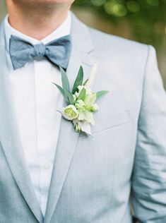 a man in a gray suit and bow tie with flowers on his lapel flower