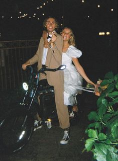 a man and woman standing next to each other on a motorcycle with lights in the background