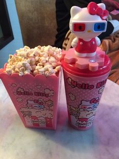 two hello kitty cups filled with popcorn on top of a table