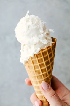 a hand holding an ice cream cone with whipped cream on top