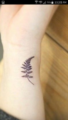 a small tattoo on the wrist of a woman's left arm with a fern