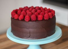 a chocolate cake topped with raspberries sitting on top of a blue plate next to a wooden table