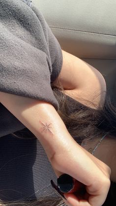 a woman with a small cross tattoo on her left arm and behind her head, sitting in a car