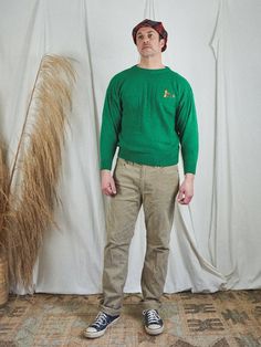 a man standing in front of a white backdrop wearing a green sweater and khaki pants