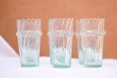 three glass vases sitting next to each other on a white cloth covered tablecloth