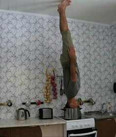 a man doing a handstand on top of a stove in a kitchen with wallpaper