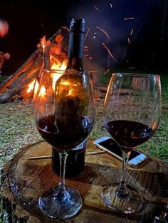 two wine glasses sitting next to each other on top of a tree stump in front of a fire