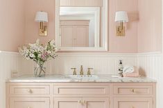 a bathroom with pink walls and marble counter tops, gold fixtures and flowers in a vase