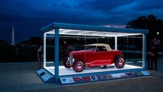 an old model car is displayed in a glass case with people standing around it at night