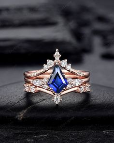 a blue and white diamond ring on top of a black stone surface with other jewelry items in the background