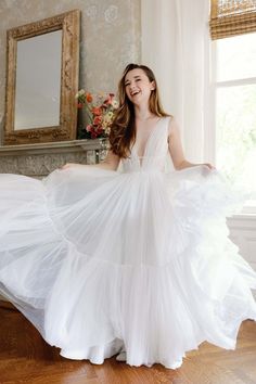 a woman in a white dress standing on a wooden floor next to a mirror and window