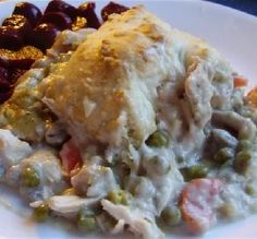 a white plate topped with meat and veggies covered in gravy next to red potatoes