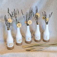 five vases with flowers in them sitting on a cloth covered table next to wheat stalks