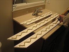 a person holding a paint roller in front of a bathroom sink and counter with three wavy lines on it