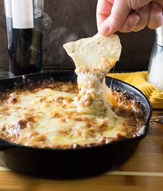 a person dipping some bread into a skillet with cheese and sauce in it on a wooden table