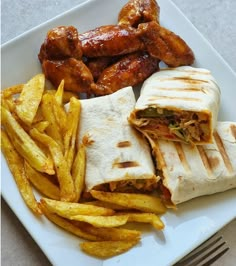 a white plate topped with a sandwich and french fries next to chicken wings on top of it