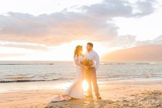 a bride and groom standing on the beach at sunset