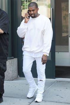 a man in white is talking on his cell phone while walking down the street with another man