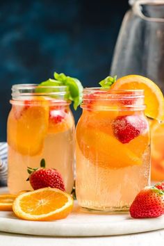 two mason jars filled with oranges and strawberries next to some sliced lemons