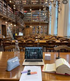 an open laptop computer sitting on top of a wooden table in a room filled with books