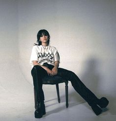 a woman sitting on top of a chair in front of a white wall with her legs crossed