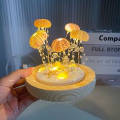 a hand holding a small yellow object with flowers on it's head and lights in the middle