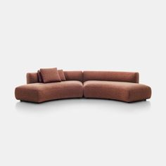 a large brown couch with pillows on it's back and side ends, sitting in front of a white wall