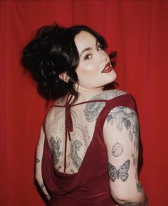 a woman in a red dress with tattoos on her arms and shoulder, posing for the camera