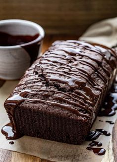 a loaf of chocolate cake sitting on top of a cutting board next to a cup of coffee