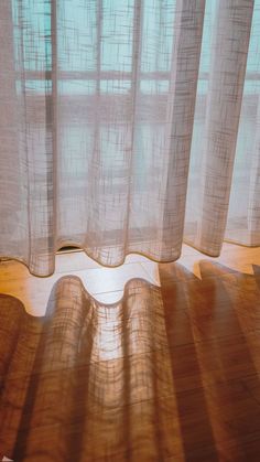 the sun shines through sheer curtains in front of a window with wood flooring