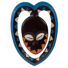 a wooden mask hanging from the side of a heart shaped wall mounted plaque with an orange, black and white face