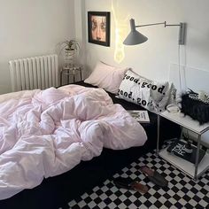 an unmade bed sitting next to a black and white checkered floor