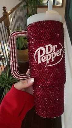 a person holding up a red cup with the word dr pepper on it in white letters