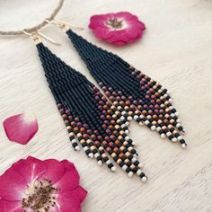 a pair of black and white beaded earrings next to pink flower