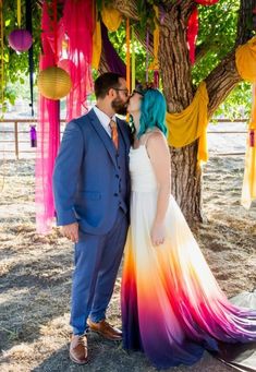 a man and woman standing under a tree with colorful streamers hanging from the trees