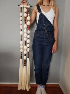 a woman standing next to a wall wearing overalls and holding two tassels