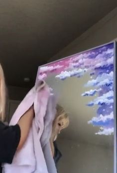 a woman is painting clouds on a large piece of art with pink and blue colors