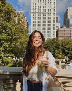 a woman holding a drink in her right hand while standing next to a railing with buildings in the background