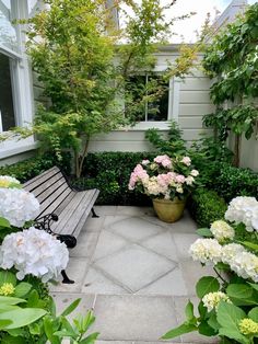 a wooden bench sitting in the middle of a garden next to some bushes and flowers