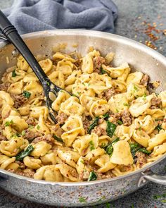 a skillet filled with pasta, meat and spinach on top of a table