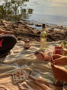 a woman sitting on the beach next to a body of water holding a bottle of wine