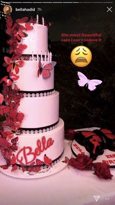 a three tiered cake sitting on top of a table with red flowers and butterflies