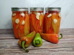 three jars filled with pickles and peppers on top of a wooden table next to a green pepper