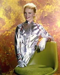 a woman sitting on top of a green chair with her hands in her pockets and smiling