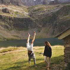 two people standing in front of a mountain with their hands up to the sky and mountains behind them