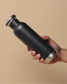 a person holding a black and silver water bottle in their left hand, on a beige background