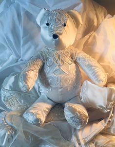 a white teddy bear sitting on top of a bed covered in white sheets and pillows