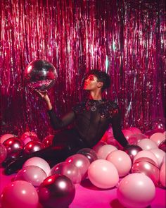 a woman sitting on the ground surrounded by balloons and streamers holding a disco ball